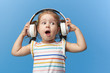 © oes - Happy smiling child enjoys listens to music in headphones over colorful bleu background. Vivid and fun emotions, happy child with pleasure listens to songs in wireless headphones