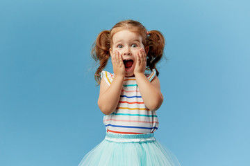 portrait of surprised cute little toddler girl child standing isolated over blue background. looking