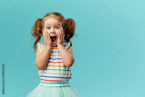 Fotografía Portrait of surprised cute little toddler girl child standing isolated over blue background