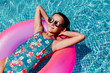 © Eva - beautiful teenager girl floating on pink donuts in a pool. Wearing sunglasses and smiling. Fun and summer lifestyle