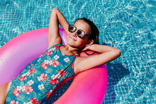 Beautiful Teenager Girl Floating On Pink Donuts In A Pool. Wearing Sunglasses And Smiling. Fun And Summer Lifestyle