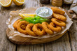 Rings of squid in batter with sauce and lemon on wooden background