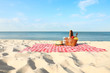 © New Africa - Checkered blanket with picnic basket and products on sunny beach