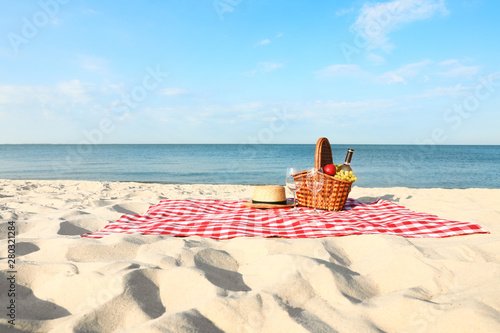Fotomural Checkered blanket with picnic basket and products on sunny beach