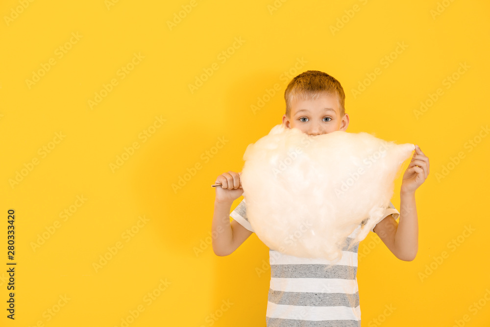 Cute little boy with cotton candy on color background