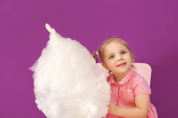 Wall Mural - Cute little girl with cotton candy sitting on chair against color background