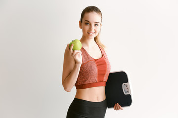 Young woman with scales and apple on light background. Weight loss concept