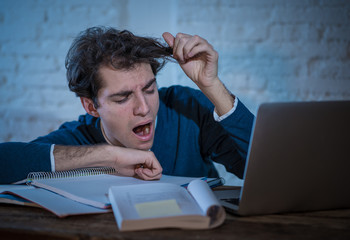 Close up portrait of a overworked and tired young man studying late at night on moody light.