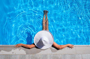 Beautiful woman with a white hat is relaxing in an infinity pool