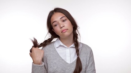 Poster - Cute thoughtful young girl winding hair on her finger while looking at the camera over white background isolated