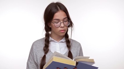 Canvas Print - Concentrated young brunette girl student reading book attentively over white background isolated