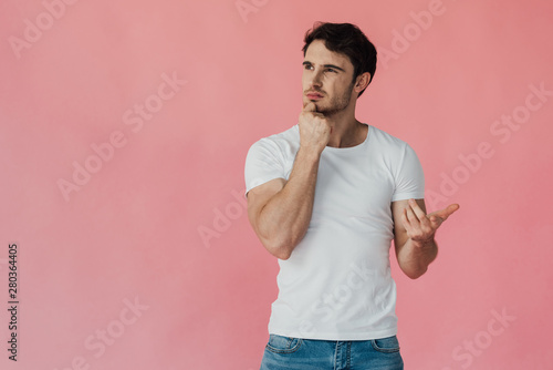 Fotografía pensive muscular man in white t-shirt propping face with fist and counting on fi