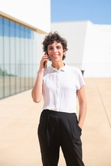 Wall Mural - Cheerful woman talking by cell phone outdoor. Happy middle aged businesswoman talking by smartphone and smiling at camera outside modern building. Communication concept