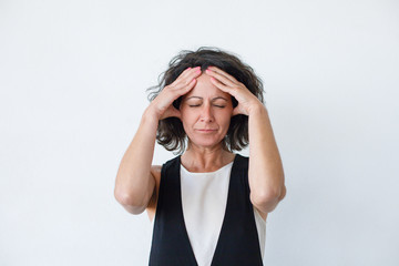 Wall Mural - Unhappy woman suffering from headache. Middle aged woman with hands on heat standing with closed eyes isolated on grey background. Emotion concept