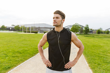 Canvas Print - Image of masculine man working out with earphones and running at green park outdoors in morning