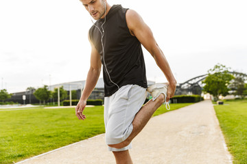 Canvas Print - Image of healthy man working out with earphones and running at green park outdoors in morning