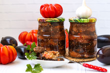 Eggplants In Acute Sauce Of Pepper, Tomatoes And Garlic In Jars On The Table, Harvest For The Winter