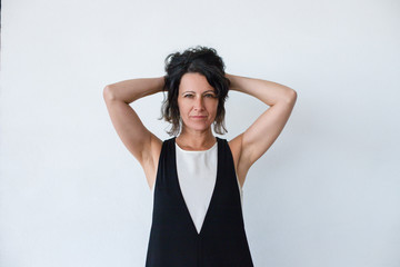 Wall Mural - Serious beautiful brunette woman. Portrait of attractive middle aged woman holding curly hair and looking at camera isolated on grey background. Beauty concept