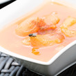 Apricot compote in a white bowl on a rattan table. On the apricot a fly is searching for food and there is a reflection of the fly in the apricot puree. The compote is served with cinnamon.