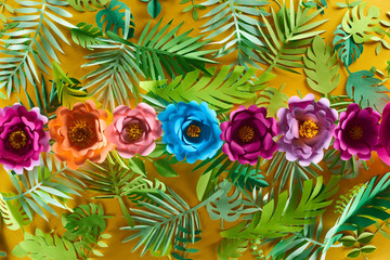 flat lay with paper cut flowers on tropical leaves on yellow bright background