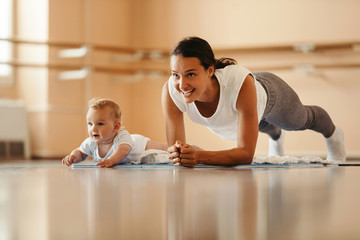 happy mother with a baby doing plank exercise in health club.