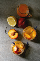 Wall Mural - Peach cold lemonade or Bellini cocktail with lavender flowers served in two glasses with pitcher of pesh juice and lemon on dark texture background. Flat lay, space. Homemade summer drink.