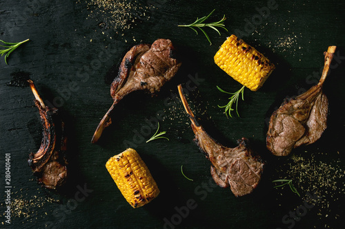 Fotomural Grilled bbq rack of lamb with sweet corn cobs and rosemary over black burned wooden background