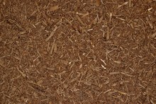 Dark Brown Wood Chip Mulch Scattered Thickly In A Landscaped Garden Area.	