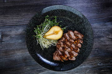 top view of grilled pork meat slices with half of baked pear