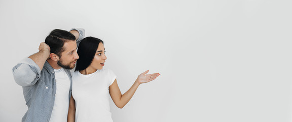 Pretty couple, man and woman emotionally advertising product pointing hand on empty background.