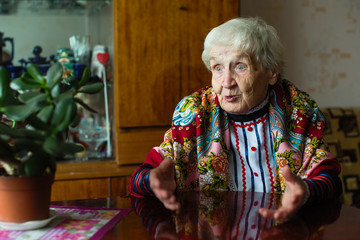 Wall Mural - An elderly woman in bright clothes gestures sitting at the table.