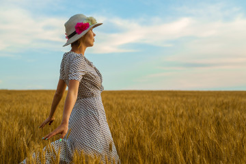 Wall Mural - Free and happy woman in a flying dress and a hat on a wheat field. Freedom, joy concept.