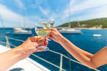 Couple holding two glasses of white wine over ocean background with yacht on background