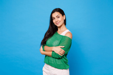 Portrait of smiling pretty young woman in green casual clothes looking camera, holding hands crossed isolated on bright blue wall background in studio. People lifestyle concept. Mock up copy space.