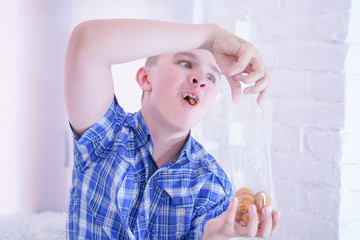 cute hungry teenager boy with fresh small bake sweets on white room background alone