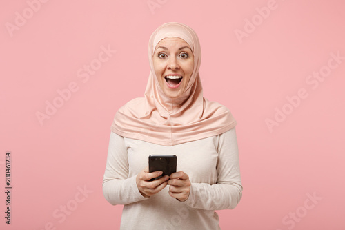 Download Surprised Young Arabian Muslim Woman In Hijab Light Clothes Posing Isolated On Pink Background People Religious Islam Lifestyle Concept Mock Up Copy Space Using Mobile Phone Typing Sms Message Stock Photo
