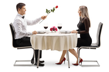 Canvas Print - Young man giving a red rose to a young woman at a restaurant table