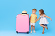 © oes - Happy kids sitting on colorful pink suitcase prepared for summer vacation. Young travelers. Little girl and boy, sister and brother, having fun isolated on blue background