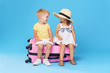 © oes - Happy kids sitting on colorful pink suitcase prepared for summer vacation. Young travelers. Little girl and boy, sister and brother, having fun isolated on blue background