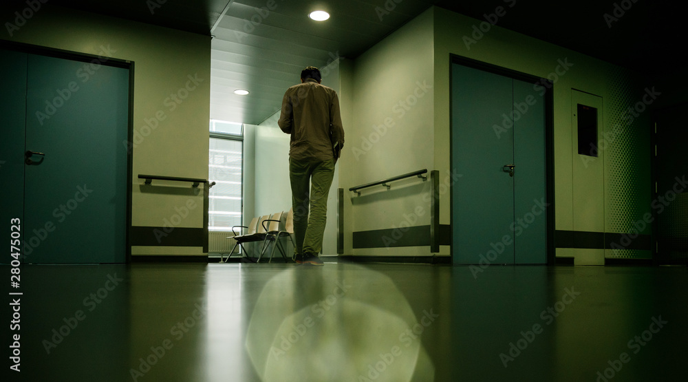 Low angle view of lonely patient in full length in modern hospital waiting lobby room walking impatiently as he waits for good or bad news from his doctor