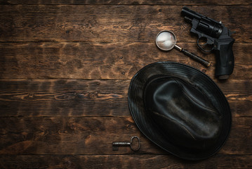 Wall Mural - detective or spy agent wooden table flat lay background with copy space. handgun, black leather hat,