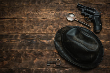 Wall Mural - detective or spy agent wooden table flat lay background with copy space. handgun, black leather hat,