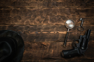 Wall Mural - detective or spy agent wooden table flat lay background with copy space. handgun, black leather hat,