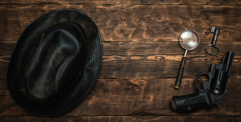 Wall Mural - detective or spy agent wooden table flat lay background with copy space. handgun, black leather hat,