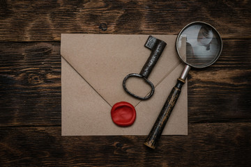 Wall Mural - old envelope with a sealing wax stamp, rusty key and a magnifying glass on a brown wooden table back