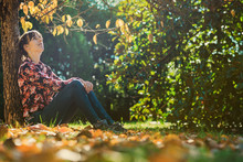 Young Woman Sitting Under An Autumn Tree
