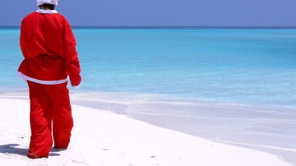 Wall Mural - Man in Santa Claus Hat walking along beach and sitting down on sand. Christmas vacation on islands