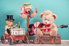 Retro Teddy Bear Toys With Play Bass Guitar On Old Luggage, Vocalist Near Golden Microphone, Bear In Cylinder Hat Playing The Drum. Rock Or Metal Music Concept. Vintage Nostalgia Style Filtered Photo