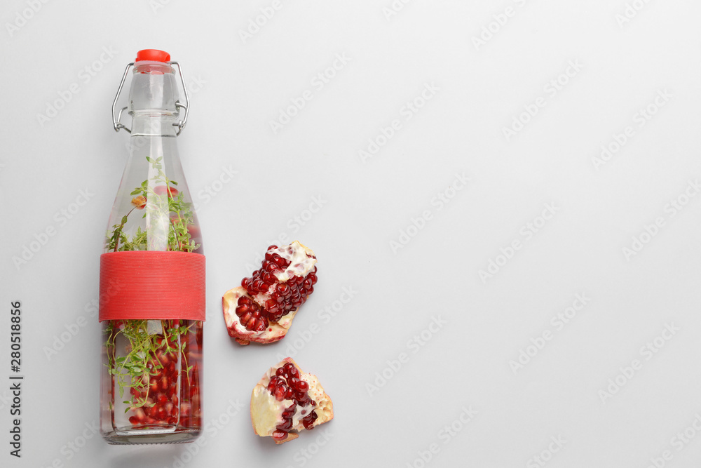Bottle of infused water and pomegranate on light background