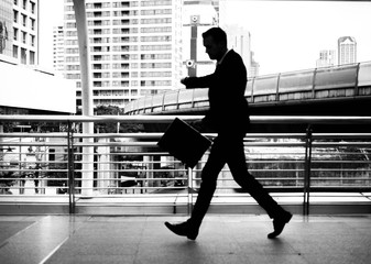 Businessman walking on the skywalk hastily. In his hand is a black leather briefcase. with flare light.